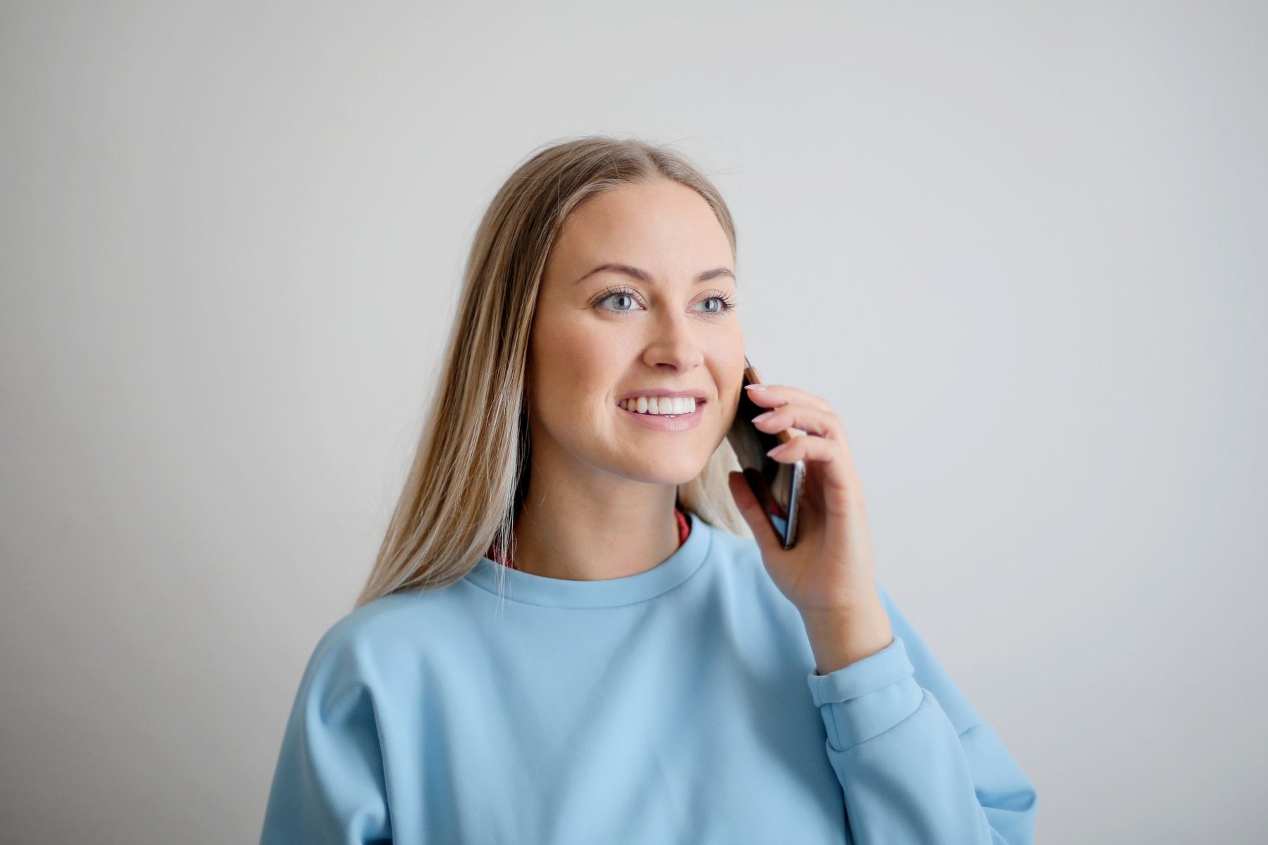 Rapariga de camisola azul a sorrir ao telemóvel, numa chamada